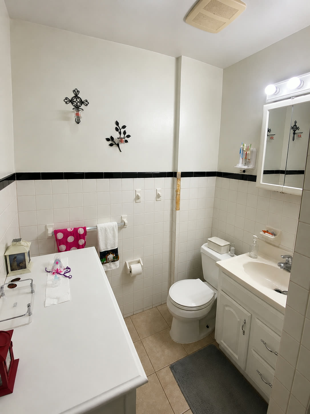 Original bathroom before renovation with dated white tile, black trim border, and builder vanity
