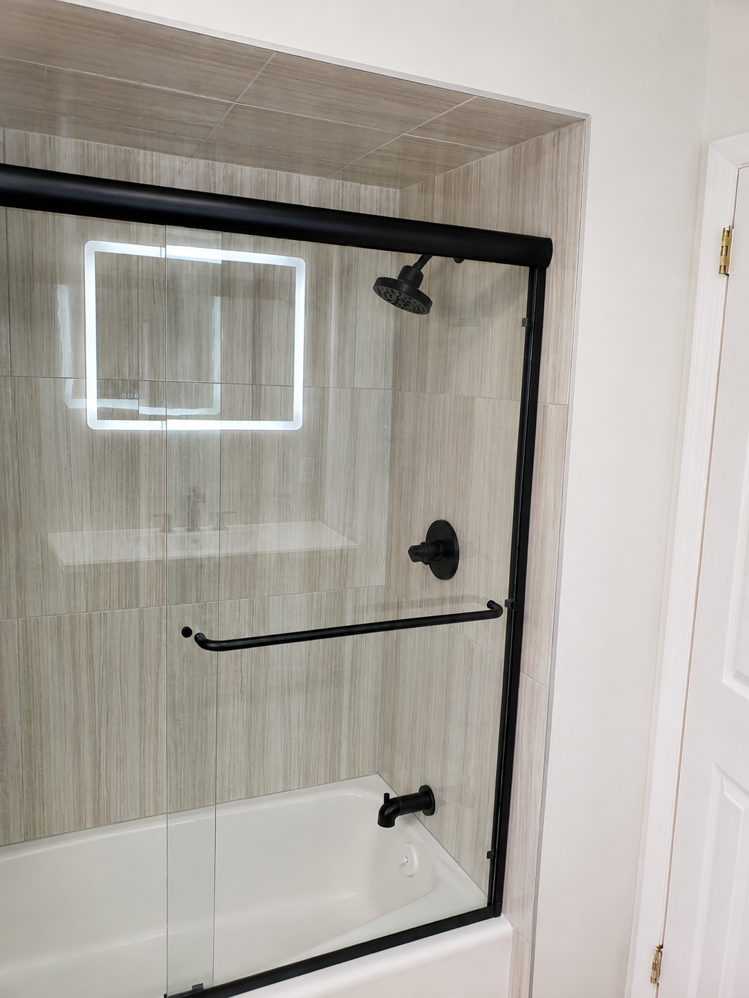 Finished tub and shower with large-format stone-look tile, glass sliding door, and matte black fixtures