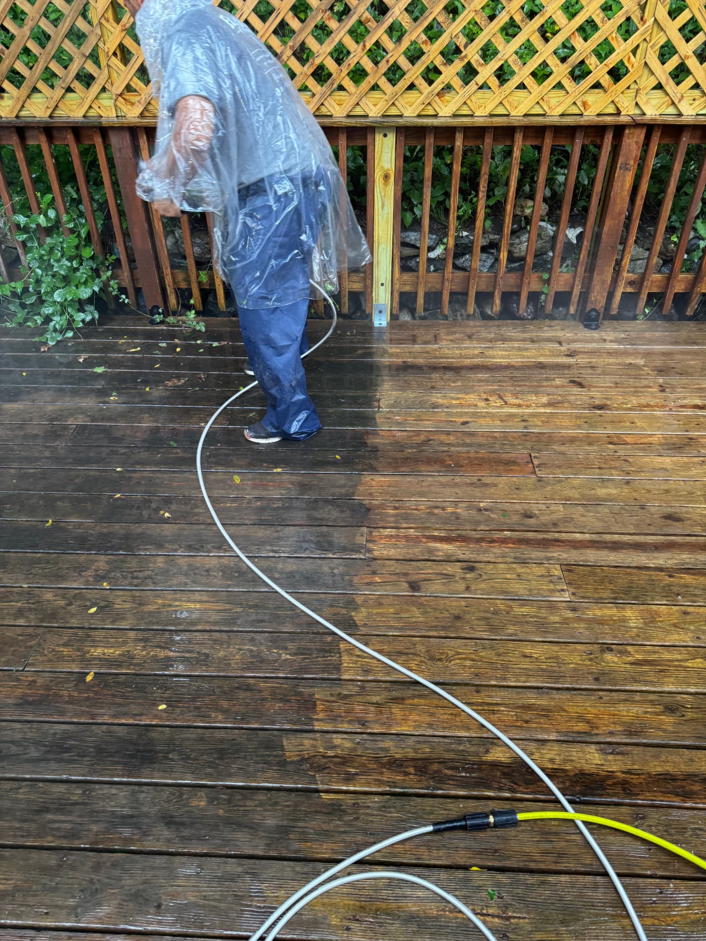 Technician pressure washing a wood deck, showing the clean surface line against the dirty boards