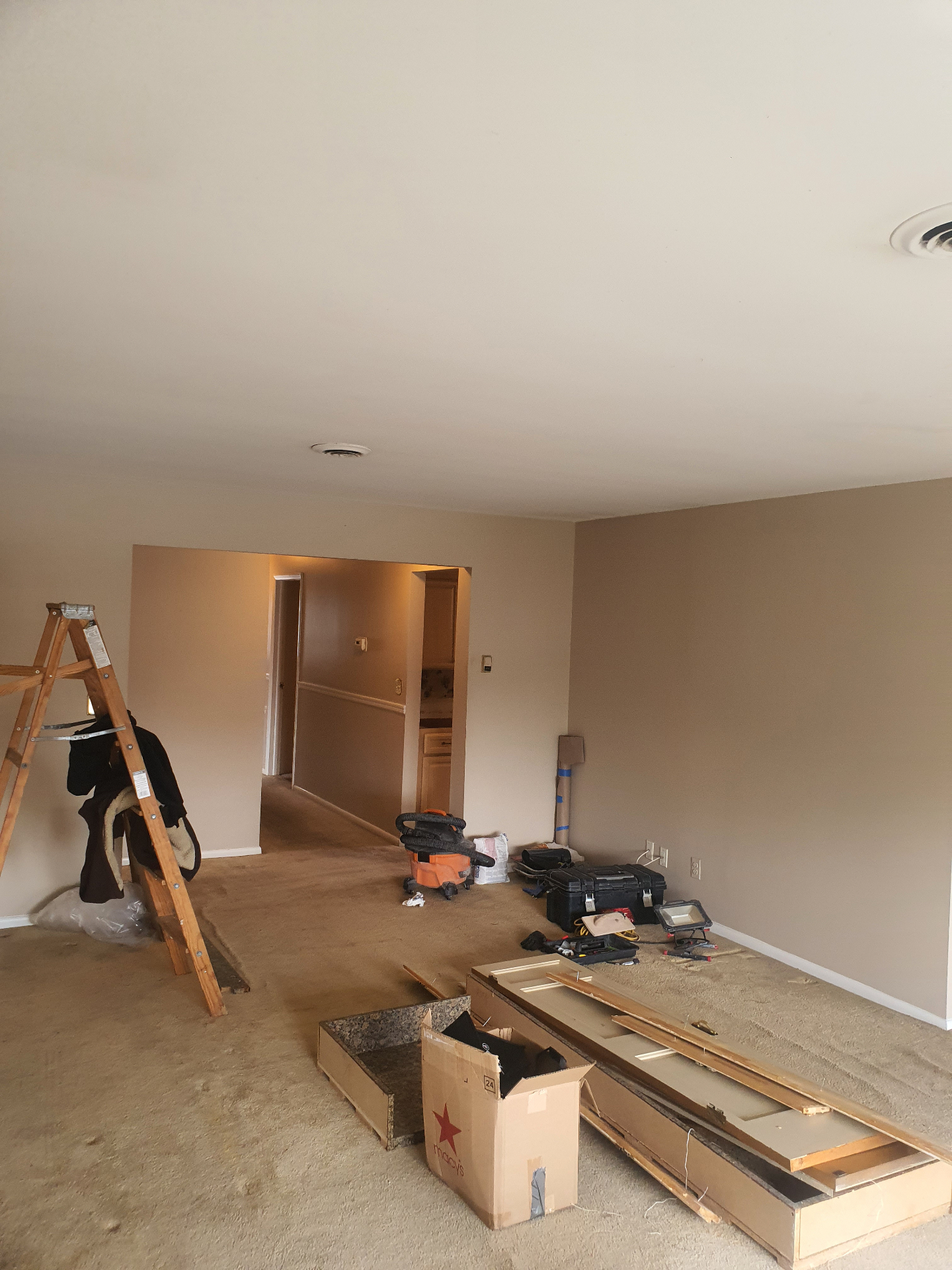 Living and dining area before interior renovation in Hasbrouck Heights, New Jersey — original carpet, dated paint, and demolition in progress with tools and ladder