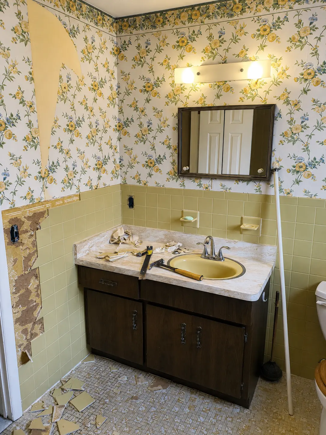 Dated bathroom before renovation with floral wallpaper, yellow tile wainscot, and dark wood vanity