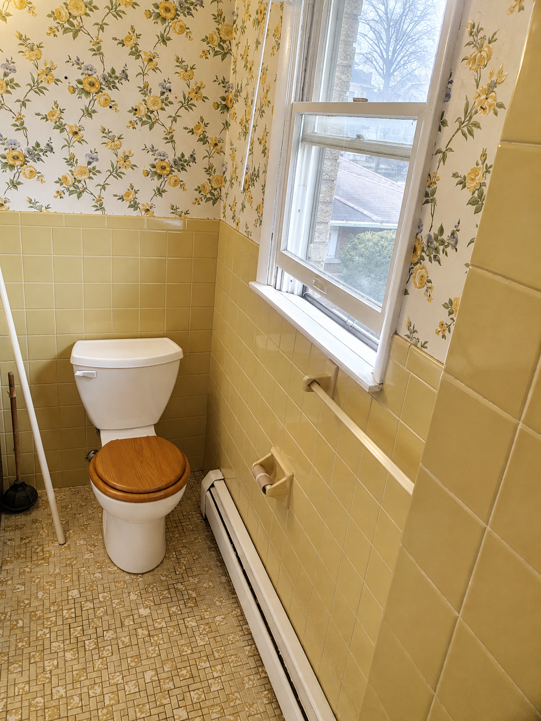 Original bathroom toilet area with yellow tile walls and patterned vinyl flooring before renovation